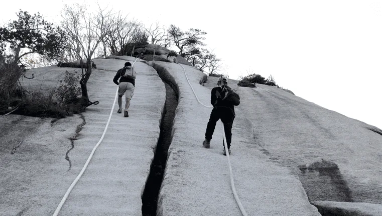 로프를-잡고-거대한-기차바위를-오르는-사람들