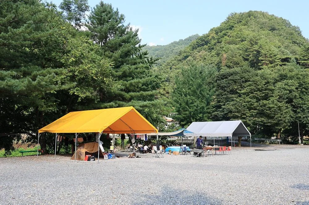 캠핑장의-타프-아래에서-사람들이-바베큐를-굽고-있다.