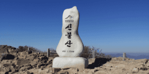 푸른-하늘-배경으로-신불산-정상석이-보여지고-있다.